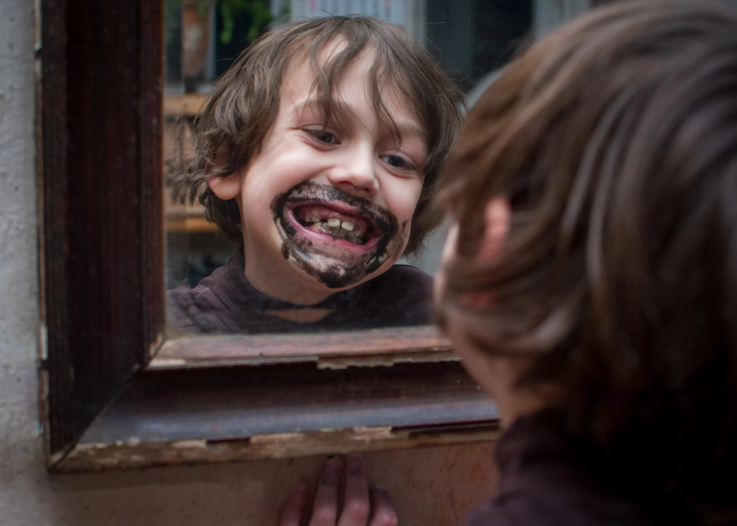 Happy boy smiling in the mirror with chocolate on his teeth, highlighting cavity awareness