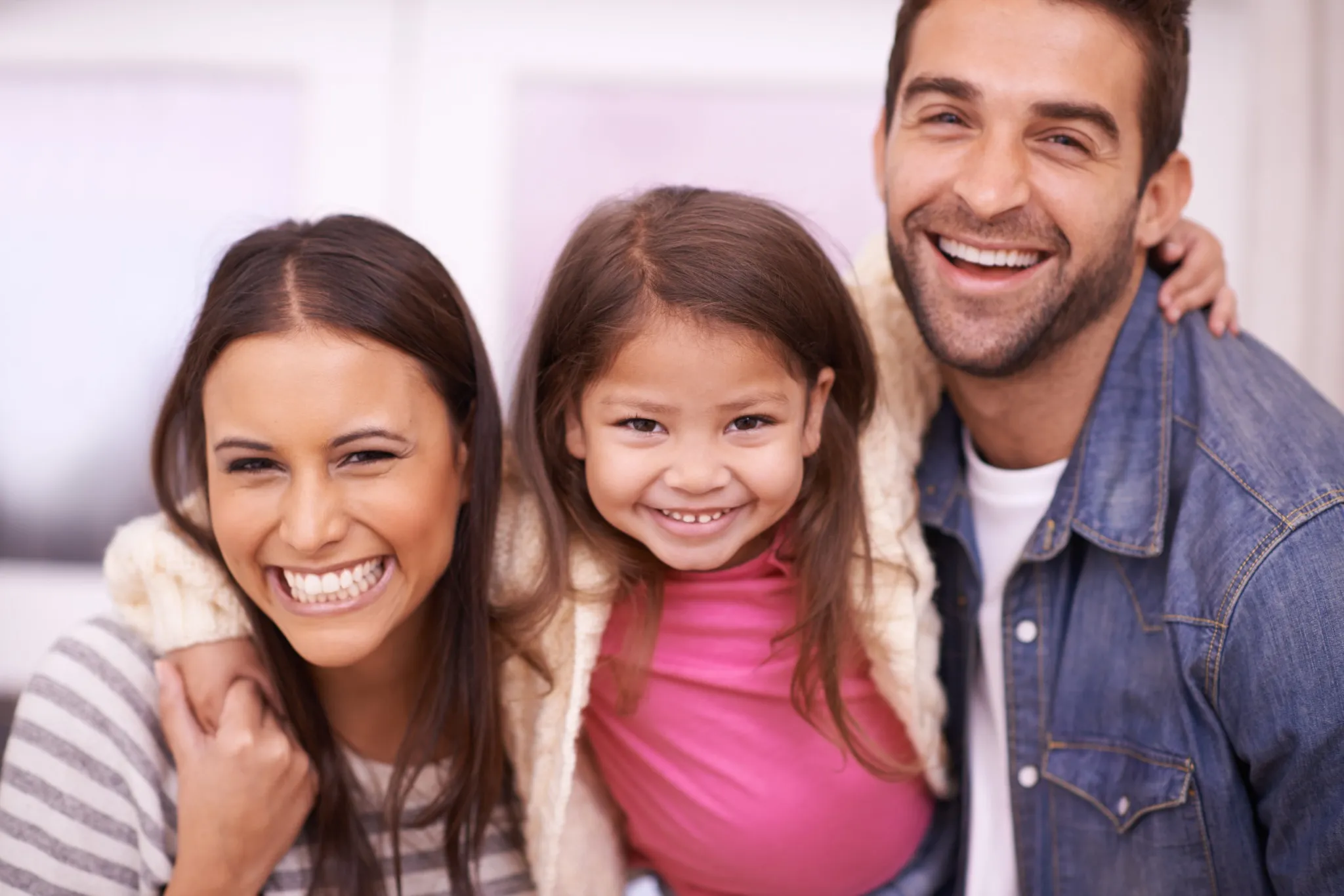 Parents and daughter smiling indoors with visible healthy teeth