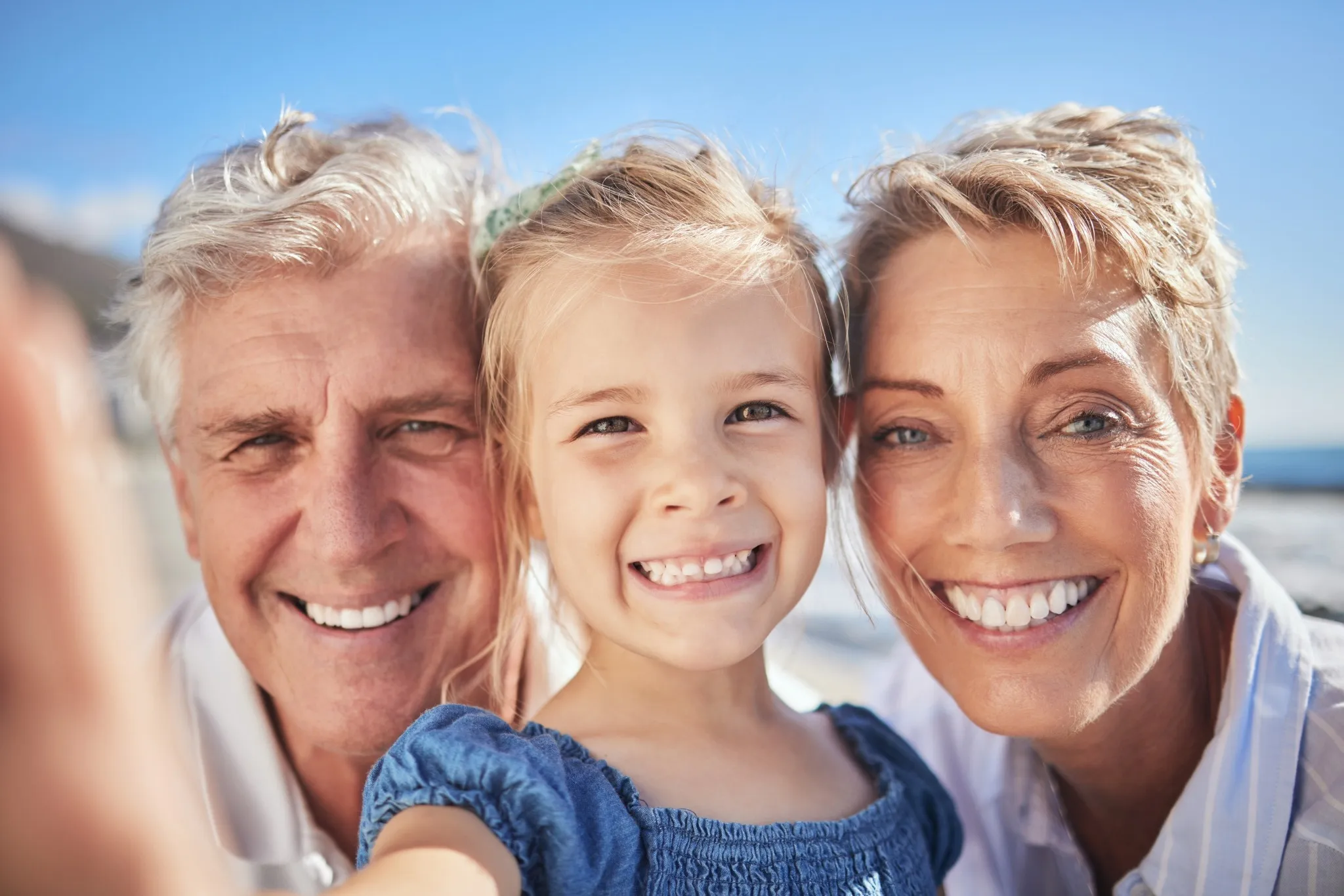 Elderly couple and young girl smiling outdoors after dental treatment