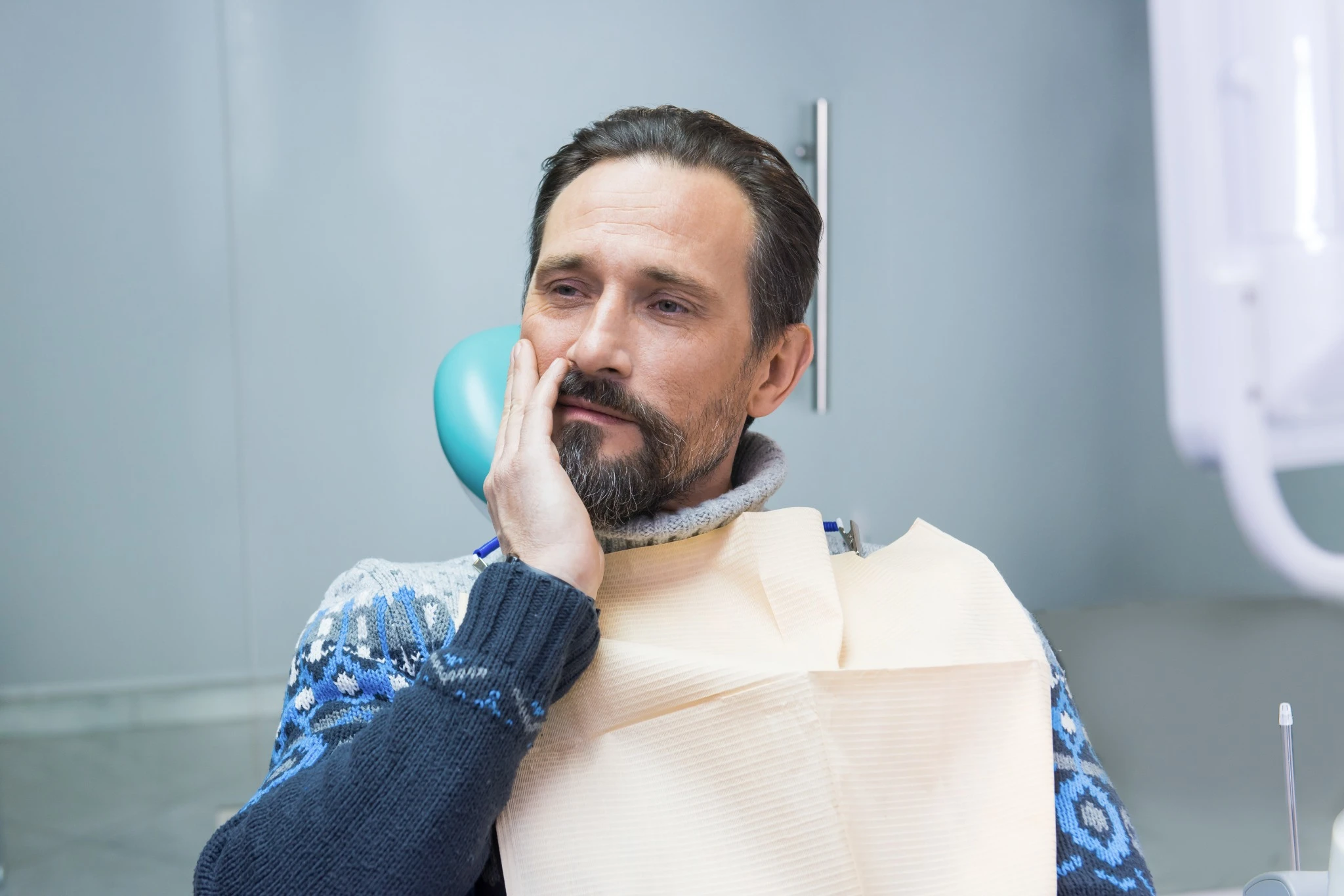 Blog 22 Adult man holding his jaw at the dentist, showing post-surgery discomfort after wisdom tooth removal